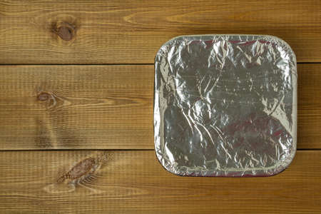 Pan with food wrapped in aluminum foil on wooden table.の写真素材