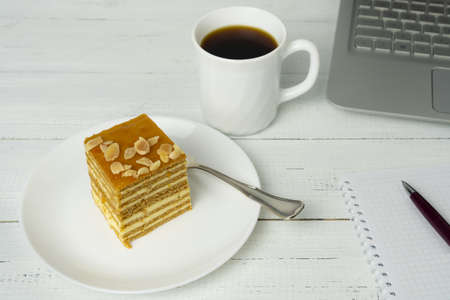 Workplace with cake on the plate, cup of coffee and laptop on wooden table. Concept of coffee break and relaxation.の写真素材