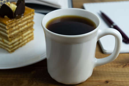 Cup of coffee close up and cake on the plate on wooden table. Concept coffee break and relaxation.
