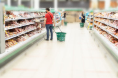 Blurred aisle and shelves in supermarket with customers. Refrigerator with meat products and sousages section.の写真素材