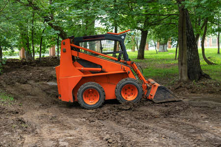Mini bulldozer or skid steer loader working with earth in public park and performing landscaping works.の写真素材