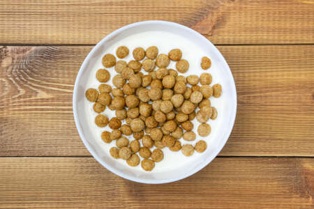White ceramic bowl with yogurt and cereal breakfast balls on wooden background, top view.
