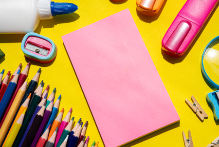 Vertical image of assorted colorful school supplies on a vibrant yellow background. In the center, a pink elongated sheet of paper for custom text or message. Perfect for back-to-school designs, education banners, or creative stationery advertising.の写真素材