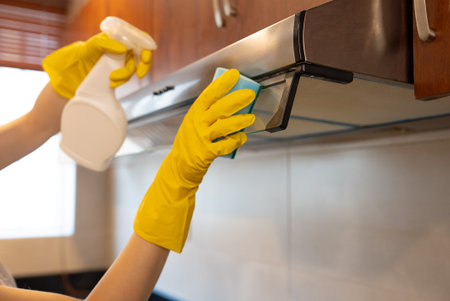 Woman in gloves using spray cleaner under cabinet. Household chores and hygiene. Cleaning service concept.の写真素材
