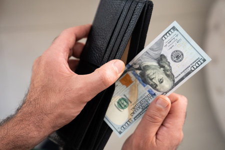 Hand pulling one US 100 bill from wallet. Concept of expense, payment, banking, or budget...