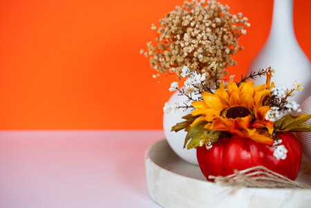 Beautiful autumn bouquet with sunflowers and dried flowers in red vase on orange background. Seasonal and festive still life.の写真素材