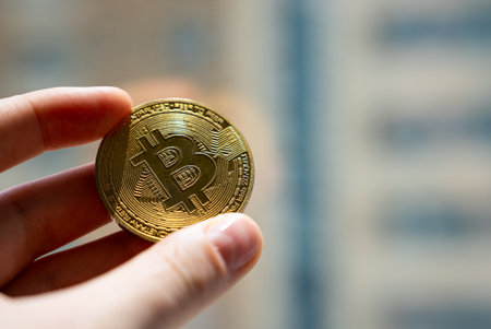 Golden Bitcoin coin held by fingers close-up, symbol of digital assets, blockchain technology, and modern cryptocurrency finance.の写真素材