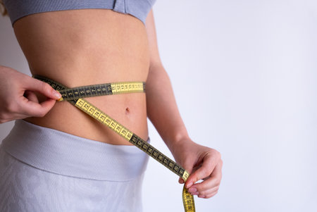 Close-up side shot of woman measuring waist with tape. Weight loss, body measurement, progress tracking and slimming concept.の写真素材
