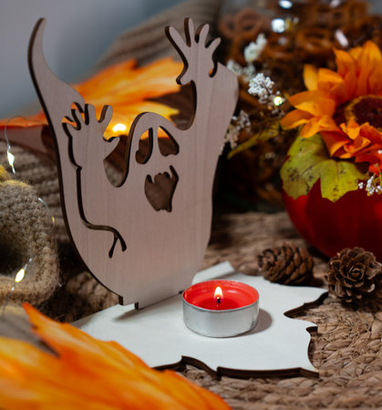 Wood ghost silhouette with small red tealight on a textured knitted surface, surrounded by fall accents. Warm, cozy Halloween atmosphere.の写真素材