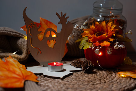 Wood ghost decor beside a red tealight and vibrant fall flowers. Warm, spooky atmosphere for October events and invitations.の写真素材