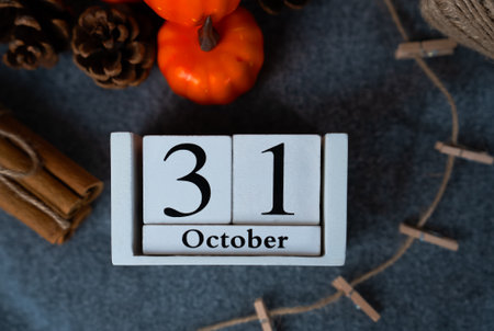 Close crop of 31 October calendar blocks on textured cloth surrounded by mini pumpkins and cinnamon,...