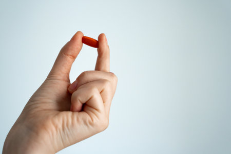 Womans hand holding a red capsule on neutral background. Concept of treatment, pharmacy, supplements...