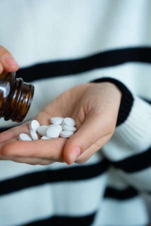 Person pouring white pills from bottle into palm. Pharmaceutical, medicine, treatment concept.