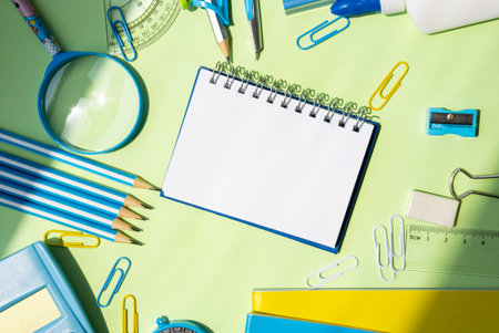 Horizontal image of a blank notebook surrounded by pencils, glue, loupes, scrapers, and partially...