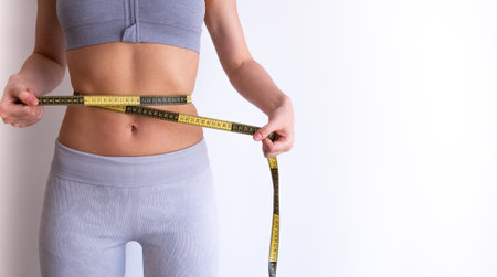 Front-facing image of woman measuring waist with tape . Lifestyle and weight-management concept for fitness and diet articles.の写真素材