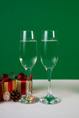 Two champagne flutes beside a wrapped present on green background, elegant holiday party concept for Christmas and New Year.の写真素材