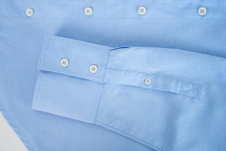 Neatly folded light blue cotton shirt with white buttons, minimal fashion and clothing concept.