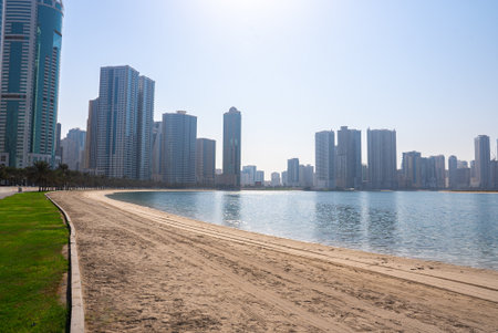 Clean beach with turquoise sea and tall skyscrapers in the distance under clear sky.の写真素材