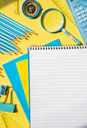Spiral notepad and stationery on yellow surface. Bright creative workspace for education, study and...