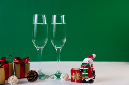Festive Christmas composition with champagne glasses, Santa figurine, and gifts on green holiday backdrop.の写真素材