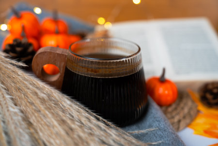 Shallow-depth coffee cup near an open book, autumn gourds and soft textiles, quiet reading moment in a fall setting.の写真素材