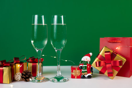Elegant champagne glasses with red and golden gift boxes on a green festive background, perfect for Christmas or New Year.の写真素材