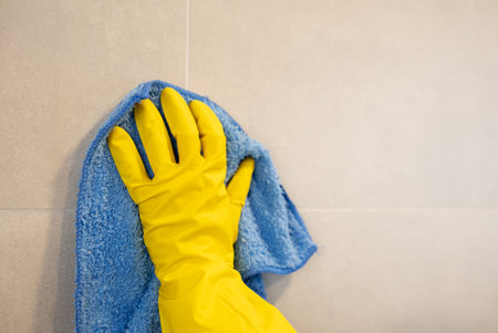 Yellow gloves holding blue cloth wiping wall surface. Household maintenance, hygiene, and cleanliness.の写真素材