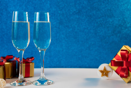 Two champagne glasses with Christmas presents and decorations on a blue background. Perfect for New Year and holiday celebrations.の写真素材