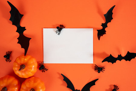Festive Halloween composition with orange pumpkins, black bats and empty sheet on orange background. Ideal for spooky invitations.の写真素材