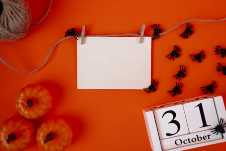 Orange flat lay with pumpkins, black spiders and blank paper card. Ideal mockup for Halloween invitations, greetings, or marketing design.の写真素材