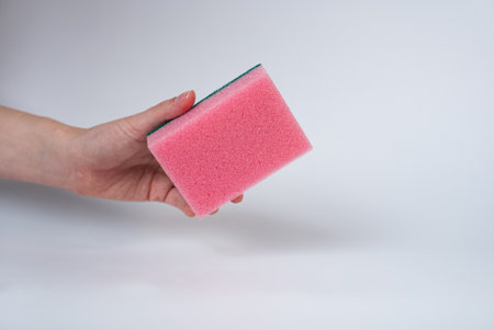 Hand holding pink cleaning sponge on white background. Household cleaning or hygiene concept, minimal style product photo.の写真素材