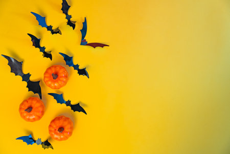 Flying black bats and pumpkins on yellow background. Festive Halloween design with copy space for seasonal greeting or party poster.の写真素材