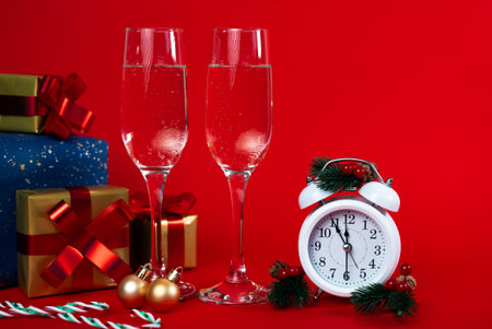 Festive New Year scene with champagne glasses, gifts, alarm clock and red background. Celebration concept.の写真素材