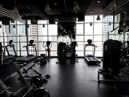 Empty modern gym with machines and free weights near large windows. Fitness center interior for wellness and healthy lifestyle concepts.の写真素材