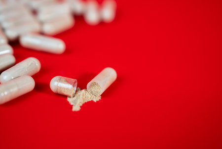 Scattered beige capsules on vivid red surface. Minimal healthcare background symbolizing medication, treatment, and supplement industry visuals.の写真素材