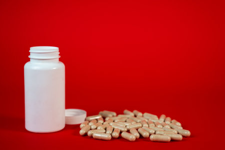 White plastic bottle with beige capsules on red background. Perfect for supplement, pharmacy, or medical marketing concepts. High quality photoの写真素材