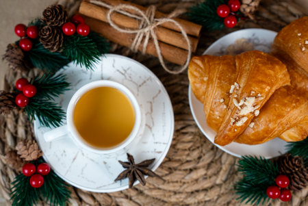 Cup of tea with croissants and festive Christmas decorations. Cozy holiday mood and warm light composition.の写真素材