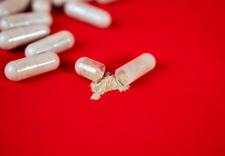 Open capsule with spilled powder on red background. Pharmaceutical and supplement concept...