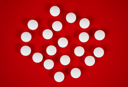 Round white tablets arranged into a decorative circle on red, abstract pharmaceutical background suitable for websites and banners.の写真素材