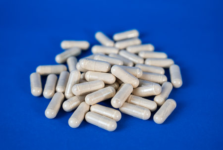 Group of white capsules lying together on a blue background. Medical and nutrition supplement...