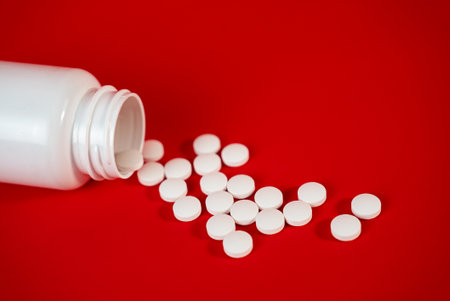 Open pill bottle with scattered white tablets on vibrant red background. Perfect for medical advertising, pharmacy visuals, or healthcare banners. High quality photoの写真素材