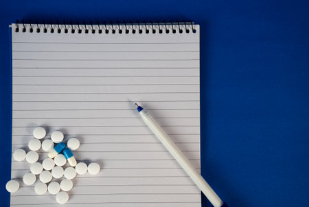 White tablets with notebook and pen on blue surface. Ideal for telemedicine, prescription notes, or healthcare education visuals.の写真素材