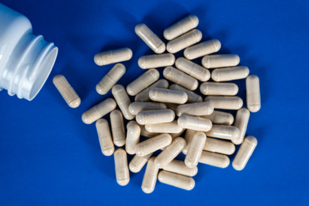 White capsules spilling from plastic bottle on blue background. Concept of healthcare, medicine, and...