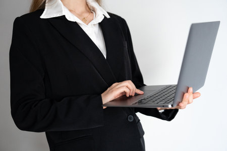 Corporate woman holding and using a laptop against a clean background. Ideal for business presentations, technology ads, and office-related visuals.の写真素材