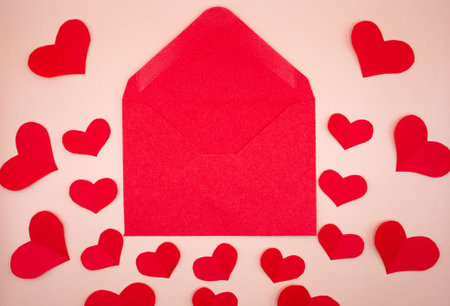 Red envelope framed with paper hearts on beige background. Valentine Day symbol for love letters,...