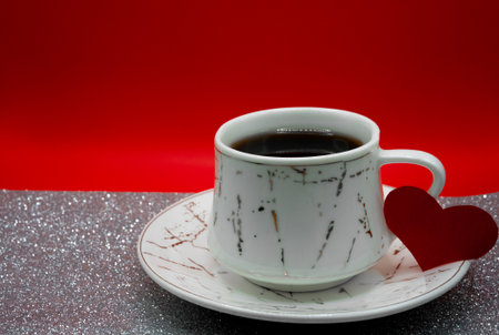 Coffee cup on saucer with red heart decoration on glitter background. Cozy Valentine Day lifestyle image with copy space for romantic messages.の写真素材