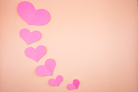 Soft Valentine Day background with pink paper hearts arranged diagonally on pastel surface. Romantic...