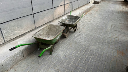Two construction wheelbarrows positioned opposite each other on a paved surface. Symbol of teamwork, logistics, manual labor and industrial workflow.の写真素材