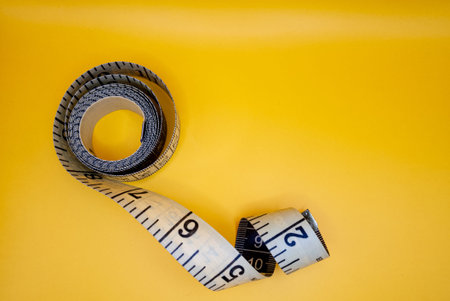 Rolled up measuring tape with markings on a bright yellow background, symbolizing measurement, tailoring, or tracking. High quality photoの写真素材