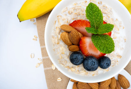 Close Up of Delicious Healthy Oatmeal Bowl with Fresh Berries, Almonds, and Mint with Bananas in...